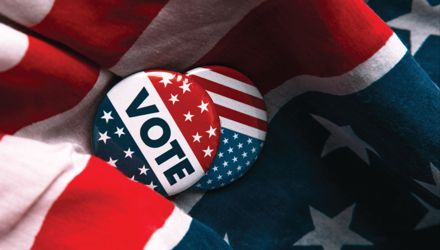 Portion of the American flag with two buttons reading "Vote" resting between the rippling of the fabric.
